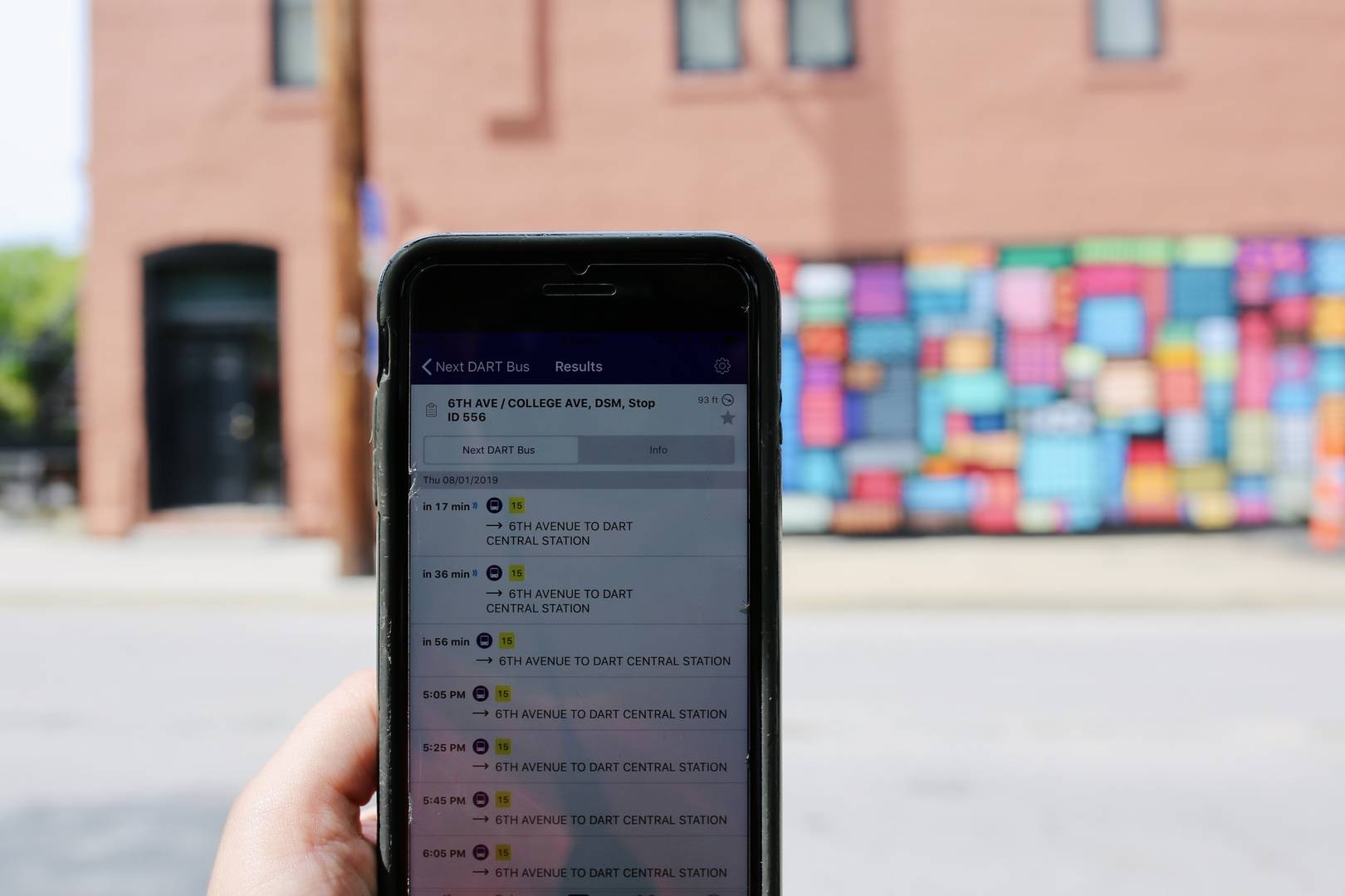 Photo of a hand holding a phone showing MyDART app in front of a mural