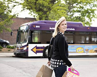 Blonde woman holding shopping bags in front of a DART bus.